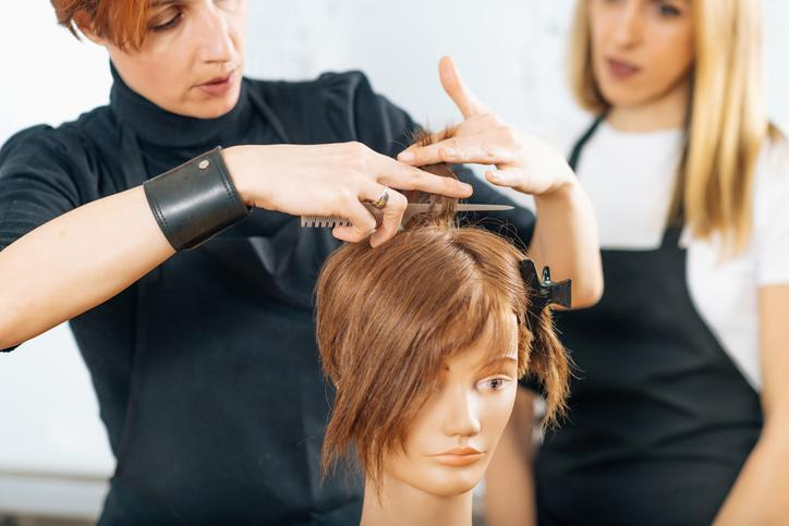 Cosmetology student practicing haircutting techniques in a salon classroom